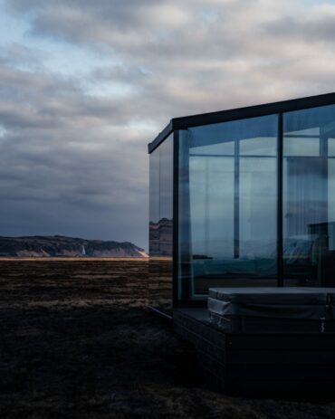 Luxury glass lodge with private Nordic bath facing a distant waterfall at dusk, Harmony Seljalandsfoss, South Iceland