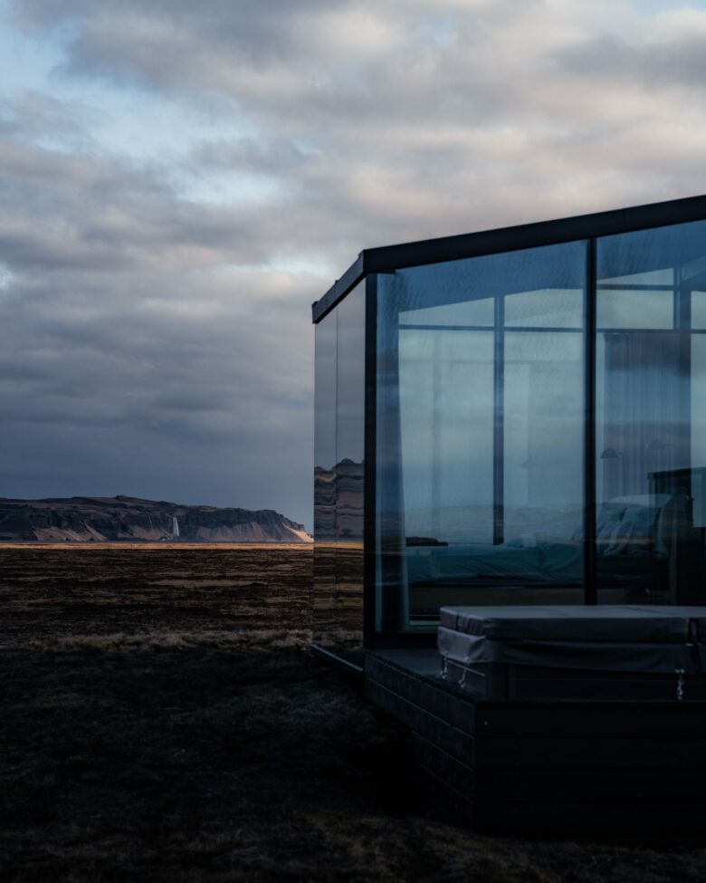 Luxury glass lodge with private Nordic bath facing a distant waterfall at dusk, Harmony Seljalandsfoss, South Iceland