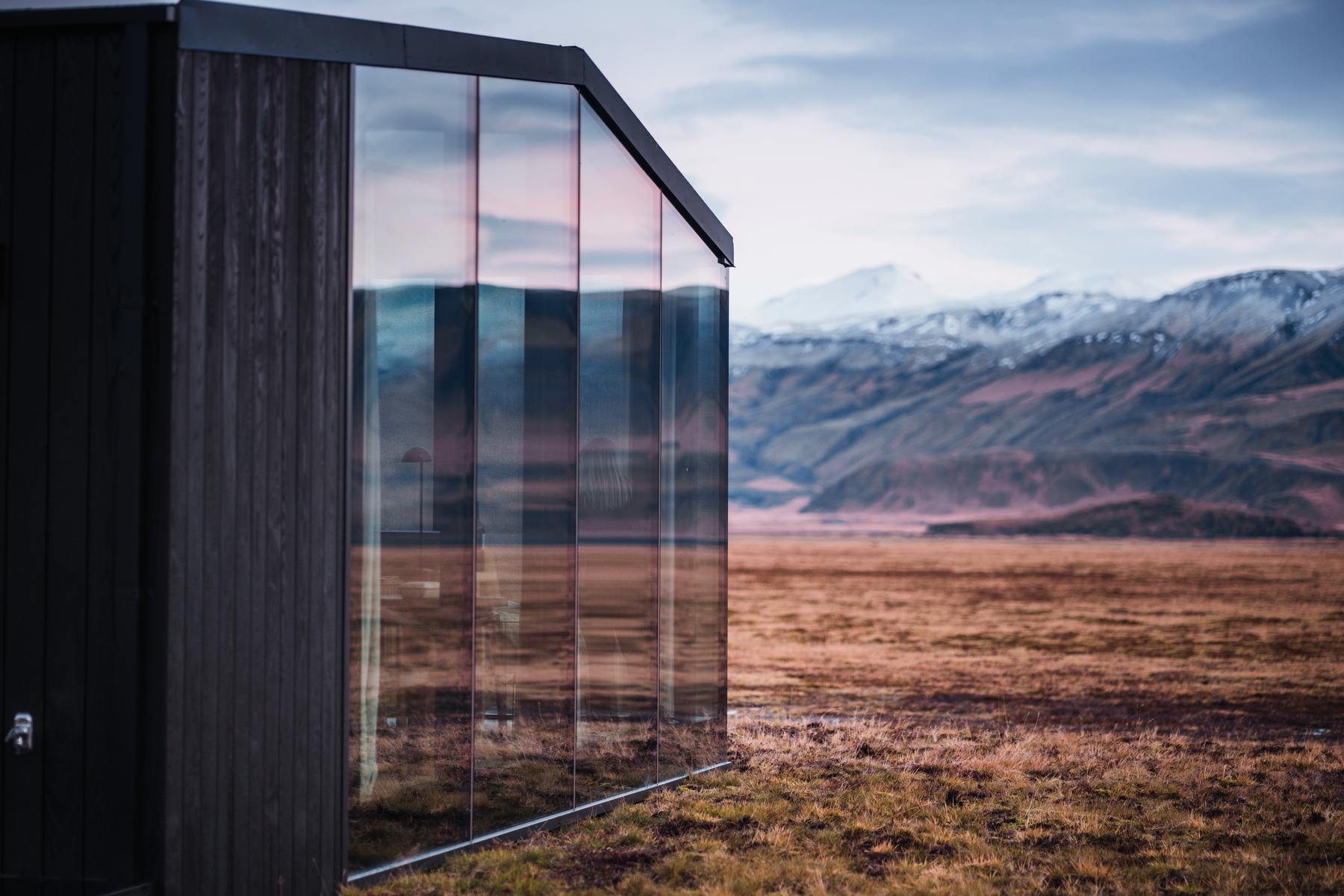 Iceland in October: glass lodge reflecting snow capped peaks and golden autumn tundra at Harmony Seljalandsfoss
