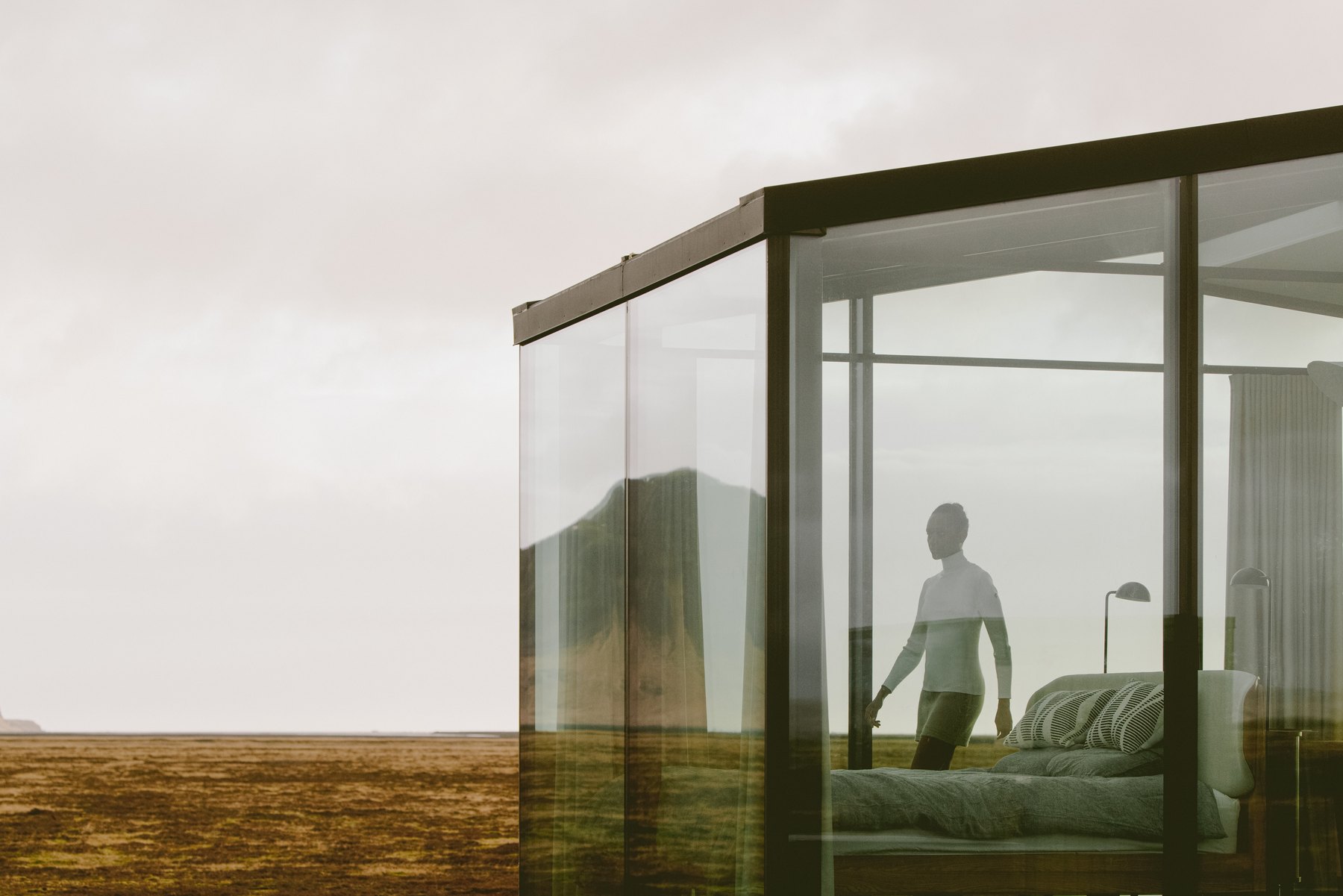 Glass walls of a Harmony Seljalandsfoss lodge with the bed visible from outside across the open tundra