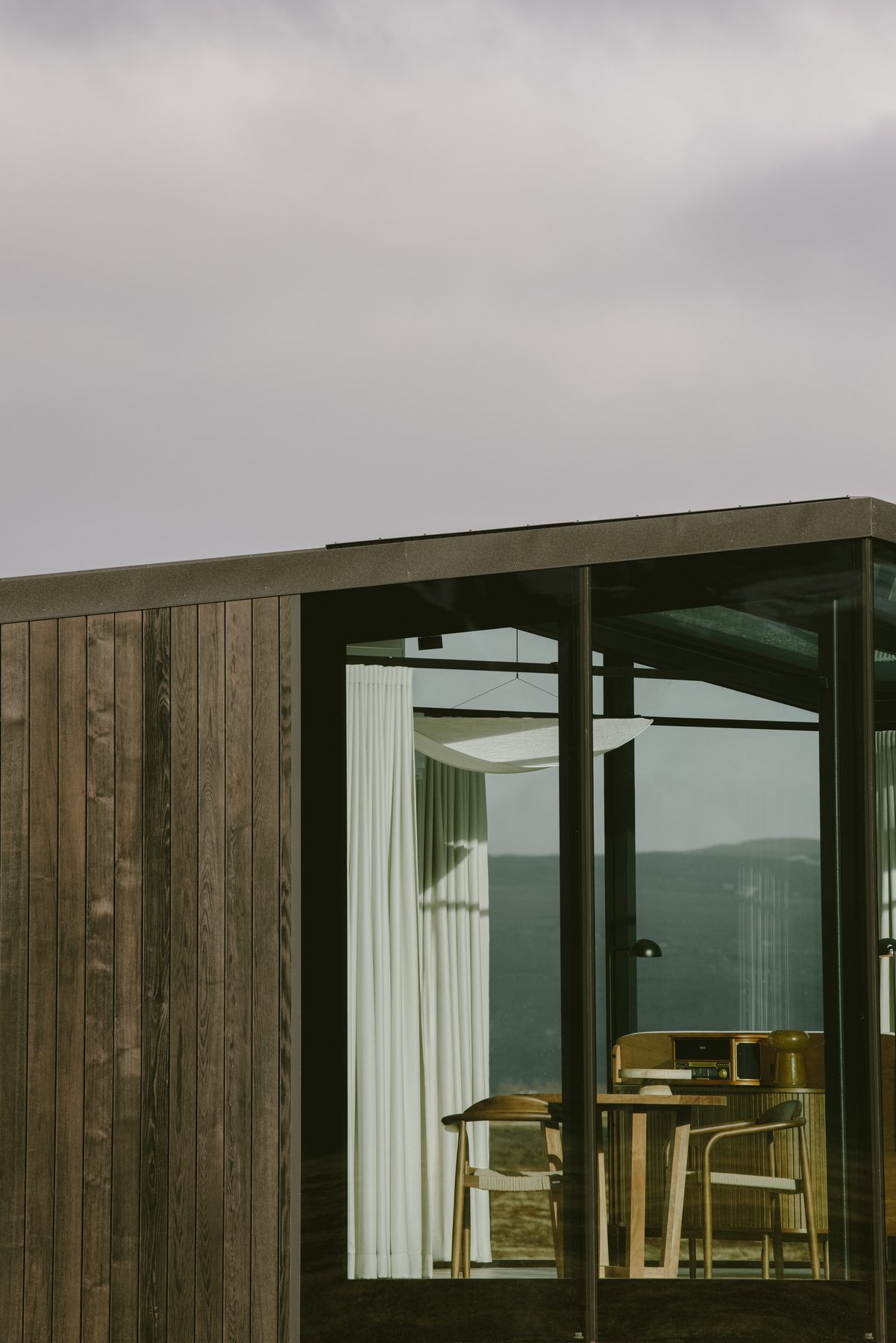 Dark timber clad wall meeting the floor to ceiling glass wall of the lodge, the two materials of the structure