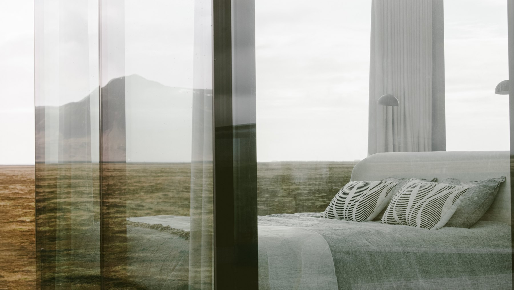 King size bed positioned against the glass wall with the Icelandic tundra directly beyond